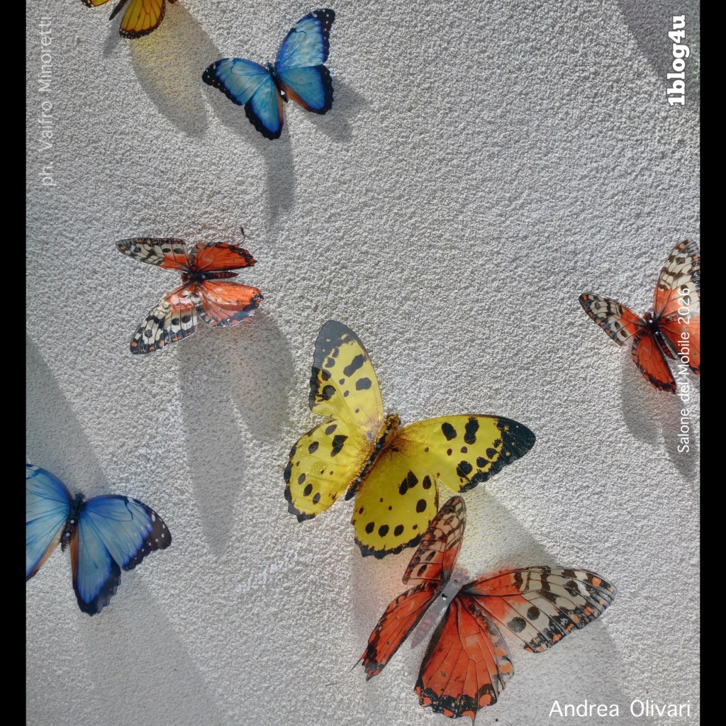 A collection of colorful butterfly sculptures mounted on a white textured wall, showcasing various species in vibrant shades of blue, yellow, orange, and red.